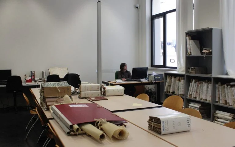 Sala di consultazione con tavoli, documenti e postazioni di lavoro